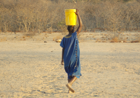 Zambian girl carrying a bucket of water on her head.