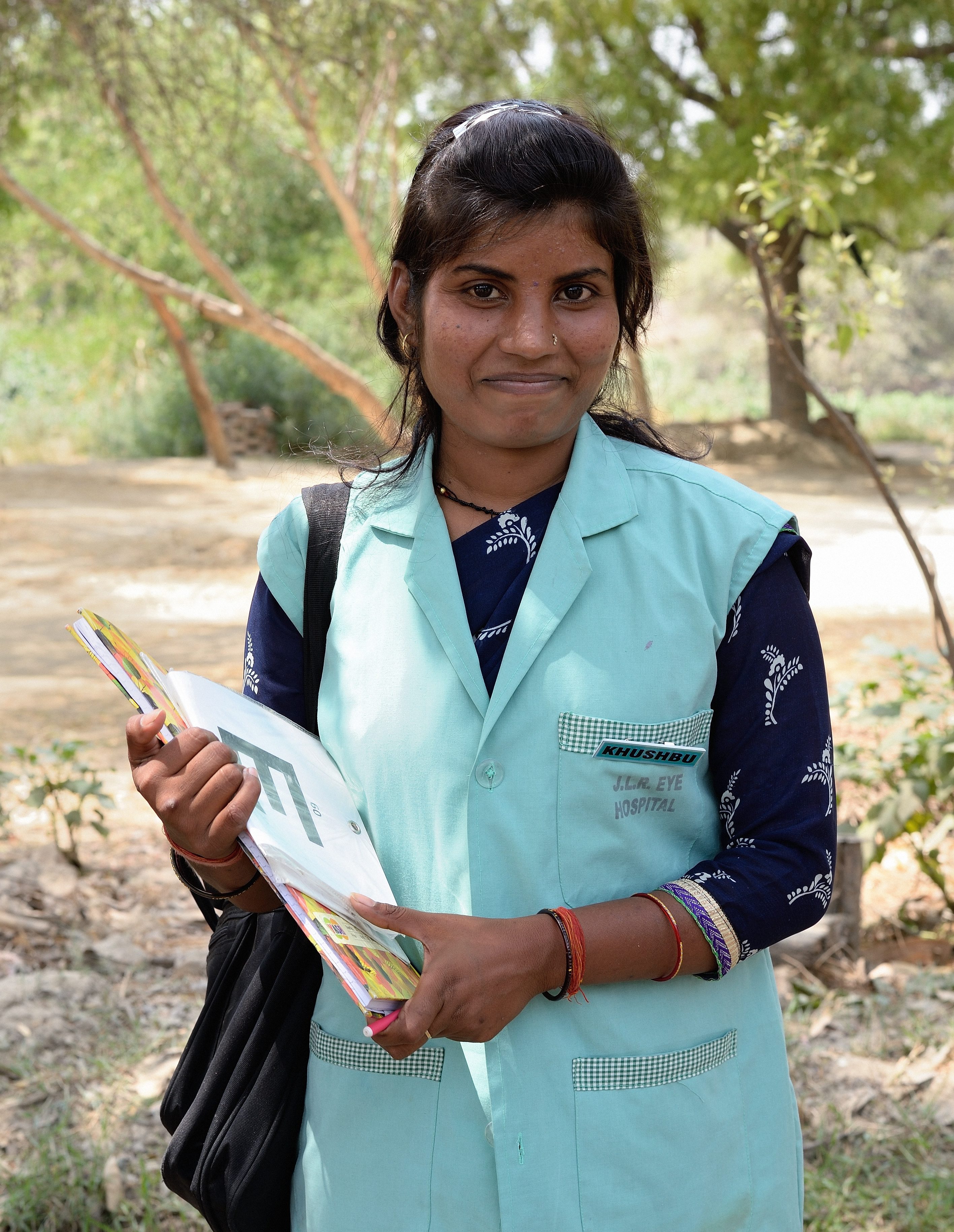 Portrait of community health worker Khushbu, she is holding a clipboard with an eye chart on it.