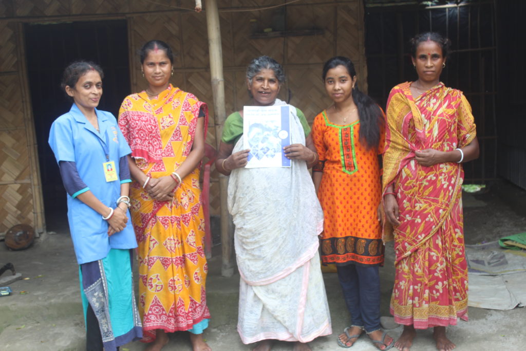 Sabitri stands with her family members and a community health worker in front of her home.