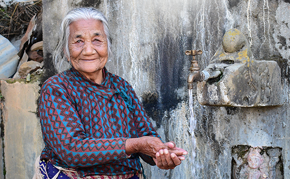 Senior woman washing hands from water faucet, in Nepal