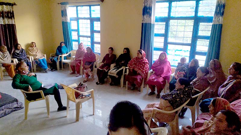 A group of women sitting around a room, paying attention to a speaker in the middle.