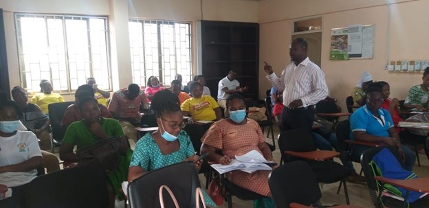 An instructor speaks to a group of students seated at desks in a classroom.