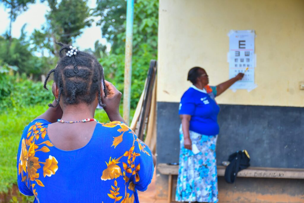 A female patient, wearing blue, faces away from the camera towards an eye exam chart. 