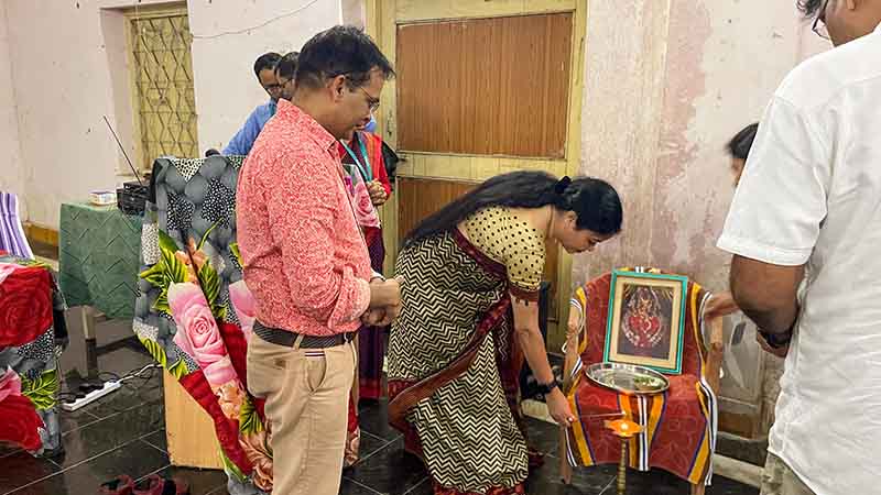 A woman in a sari leans down to light incense, as a group of people look on. 