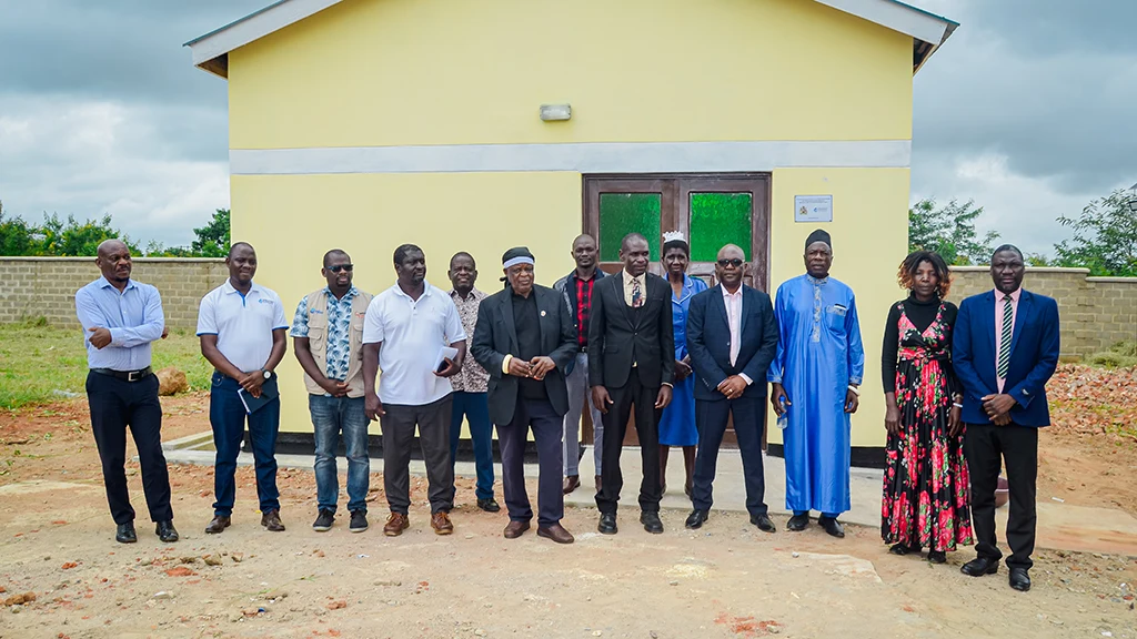 A group of men and women stand in front of a small clinic painted yellow.